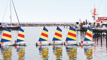 Kleine Segelboote mit bunten Segeln schippern in der Gruppe entlang der Ostseeküste