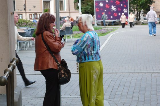 Zwei Frauen stehen auf der Straße und reden, die eine hält einen Lippenstift am Mund